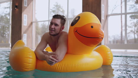 happy-caucasian-man-is-relaxing-in-swimming-pool-lying-on-big-inflatable-duck-and-floating